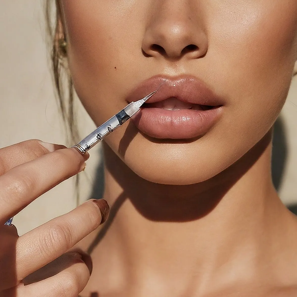 Close-up of full, smooth lips in a soft nude tone with a fine injector held at the lip border